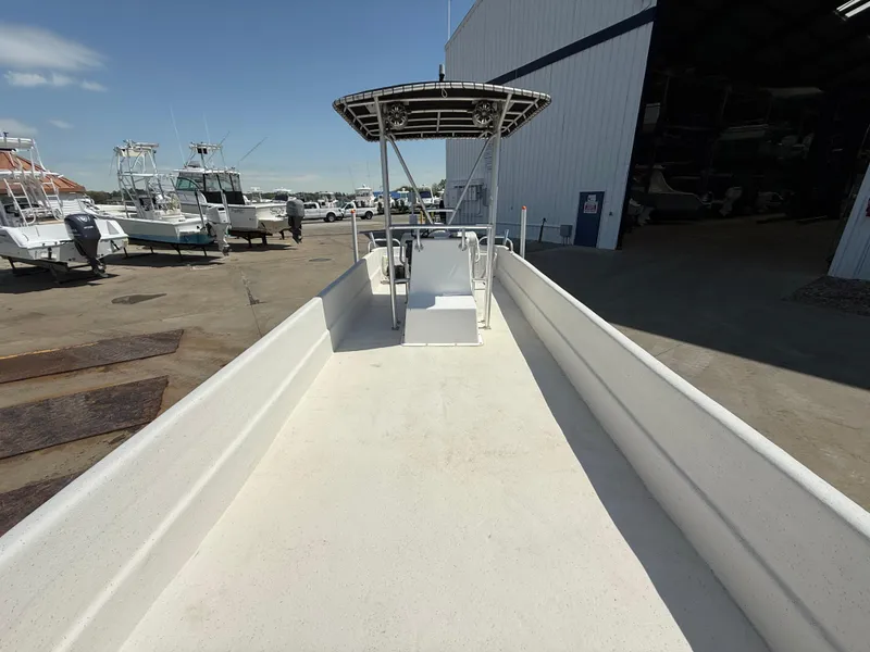 Slide: The Image of 2017 Carolina Skiff 24 DLX boat at a marina, featuring a spacious deck and T-top. - 12