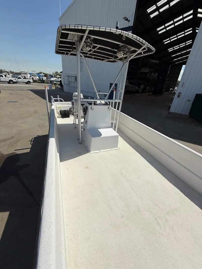 Slide: The Image of 2017 Carolina Skiff 24 DLX boat with T-top, parked near a warehouse. - 13