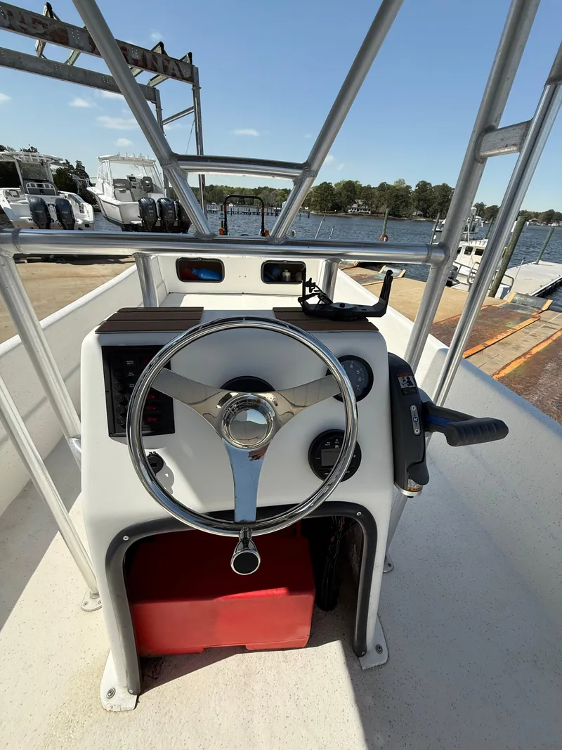 Slide: The Image of 2017 Carolina Skiff 24 DLX boat console with steering wheel and controls, docked by the water. - 9