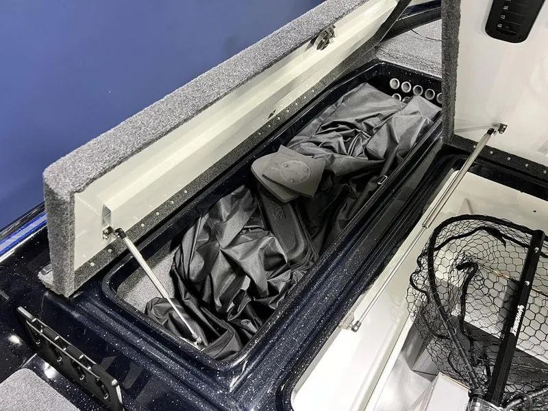 Slide: The Image of Open storage compartment in a 2025 Phoenix 920 Elite boat, featuring fishing gear and net. - 13