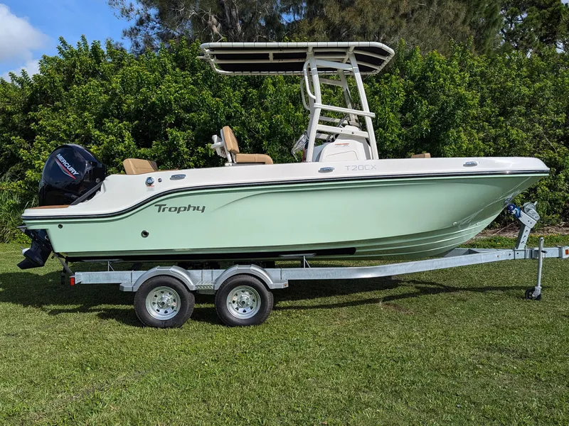 Slide: The Image of 2025 Bayliner Trophy T20CC boat on trailer, parked on grass with lush greenery background. - 1