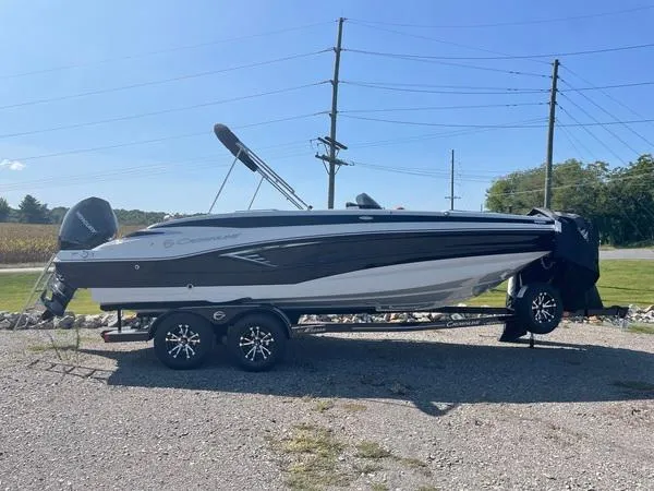 The Image of 2023 Crownline E225 XS boat on trailer, parked outdoors under clear blue sky. - 0