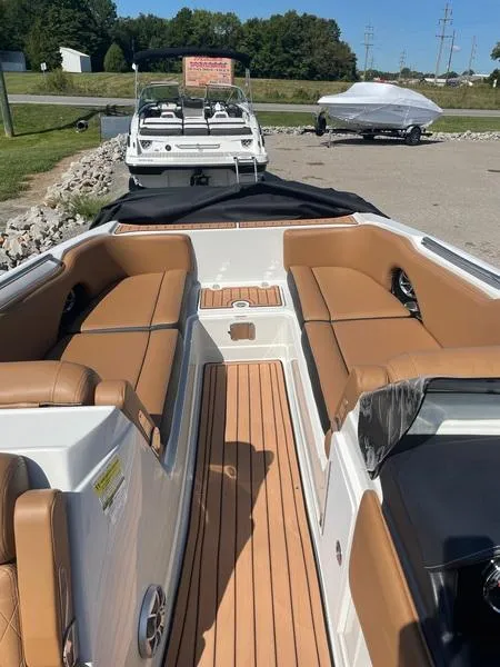 Slide: The Image of 2023 Crownline E225 XS boat with tan seating and sleek design, docked outdoors. - 7