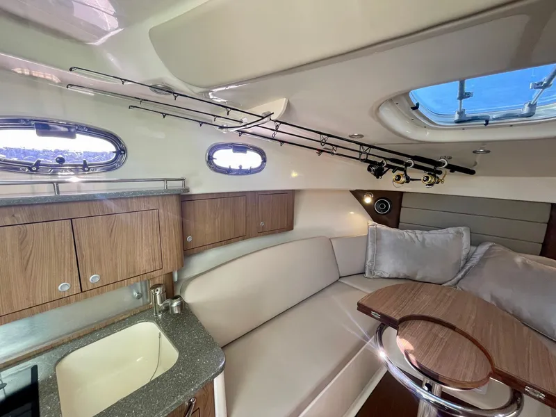 Slide: The Image of 2018 Boston Whaler 315 Conquest cabin interior with seating, table, and fishing rods. - 33