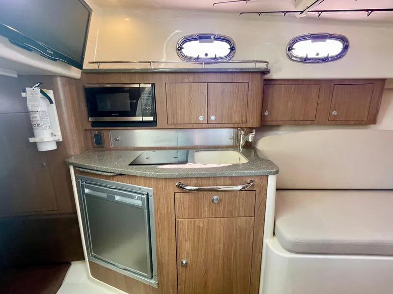 Slide: The Image of 2018 Boston Whaler 315 Conquest cabin kitchen with microwave, sink, and wooden cabinetry. - 36