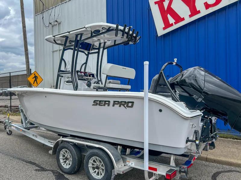 Slide: The Image of 2025 Sea Pro 225 Sandbar boat on trailer, parked outdoors near a blue building. - 2