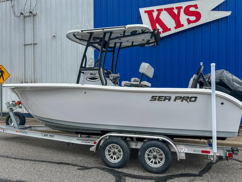 Slide: The Image of 2025 Sea Pro 225 Sandbar boat on trailer, parked outside a blue building. - 5