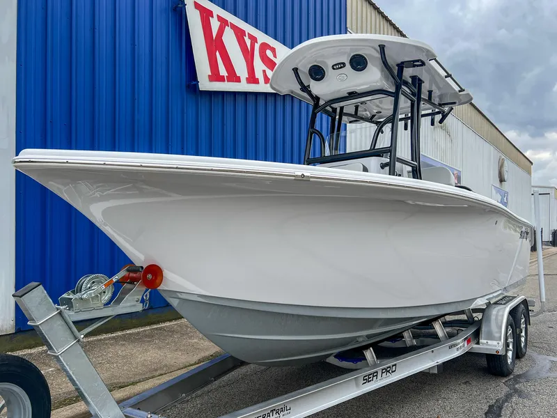 Slide: The Image of 2025 Sea Pro 225 Sandbar boat on trailer, parked outside blue building. - 6