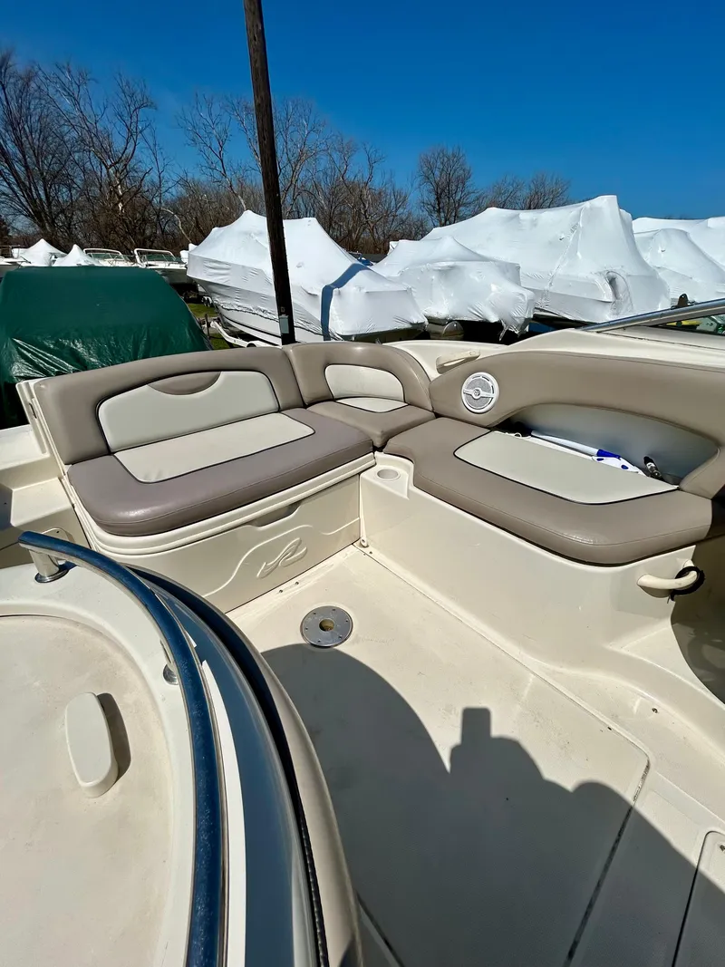 Slide: The Image of 2002 Sea Ray 270 Sundeck interior with beige seating and storage, under clear blue sky. - 8