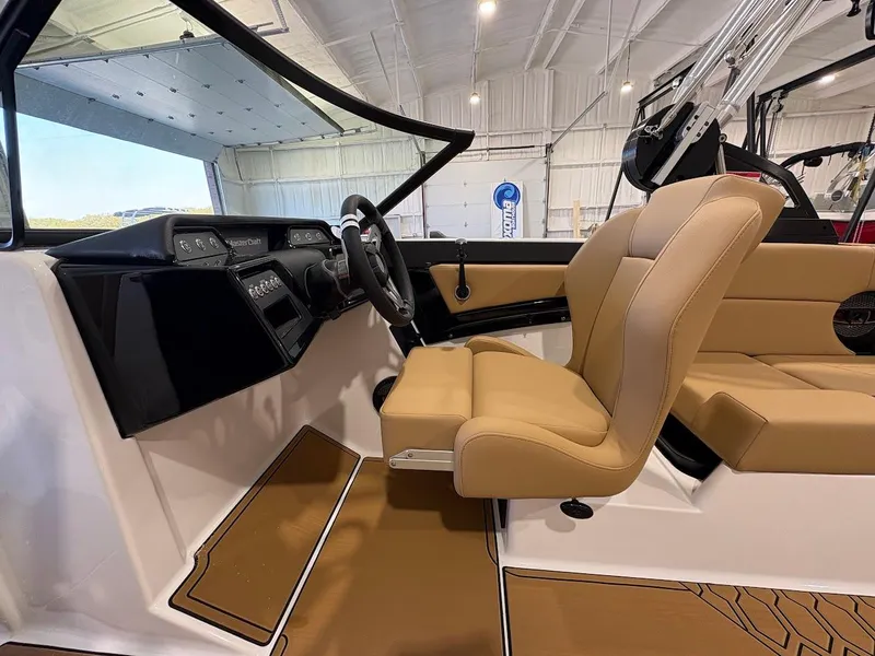 Slide: The Image of 2025 MasterCraft NXT23 boat interior with tan seats and modern dashboard in a showroom. - 12