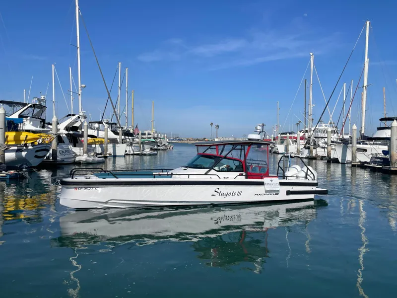Slide: The Image of 2021 Axopar 28 Brabus T-Top boat docked in a marina under clear blue skies. - 2