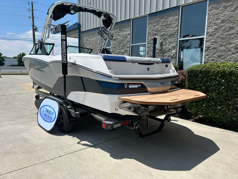 Slide: The Image of 2022 MasterCraft NXT24 boat on trailer, parked outdoors near a building. - 2
