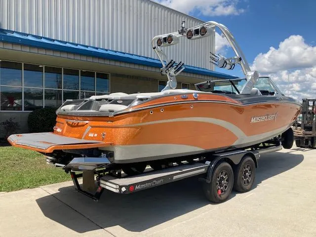 Slide: The Image of 2018 MasterCraft X26 boat in orange on a trailer, parked outdoors. - 1