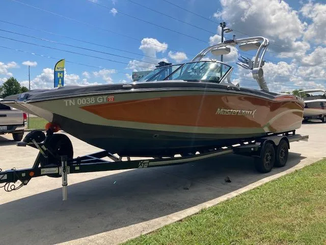 Slide: The Image of 2018 MasterCraft X26 boat on trailer, parked outdoors under a blue sky. - 2