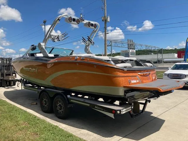 Slide: The Image of 2018 MasterCraft X26 boat on trailer, orange and silver, parked outdoors under blue sky. - 3