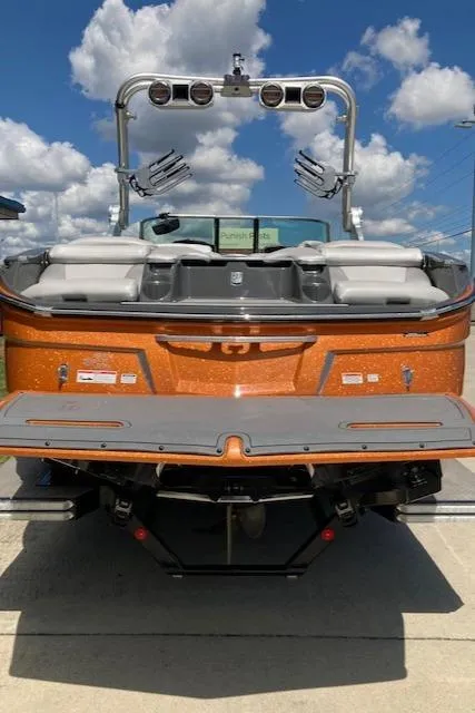 Slide: The Image of 2018 MasterCraft X26 boat with orange exterior, rear view, under a blue sky with clouds. - 4