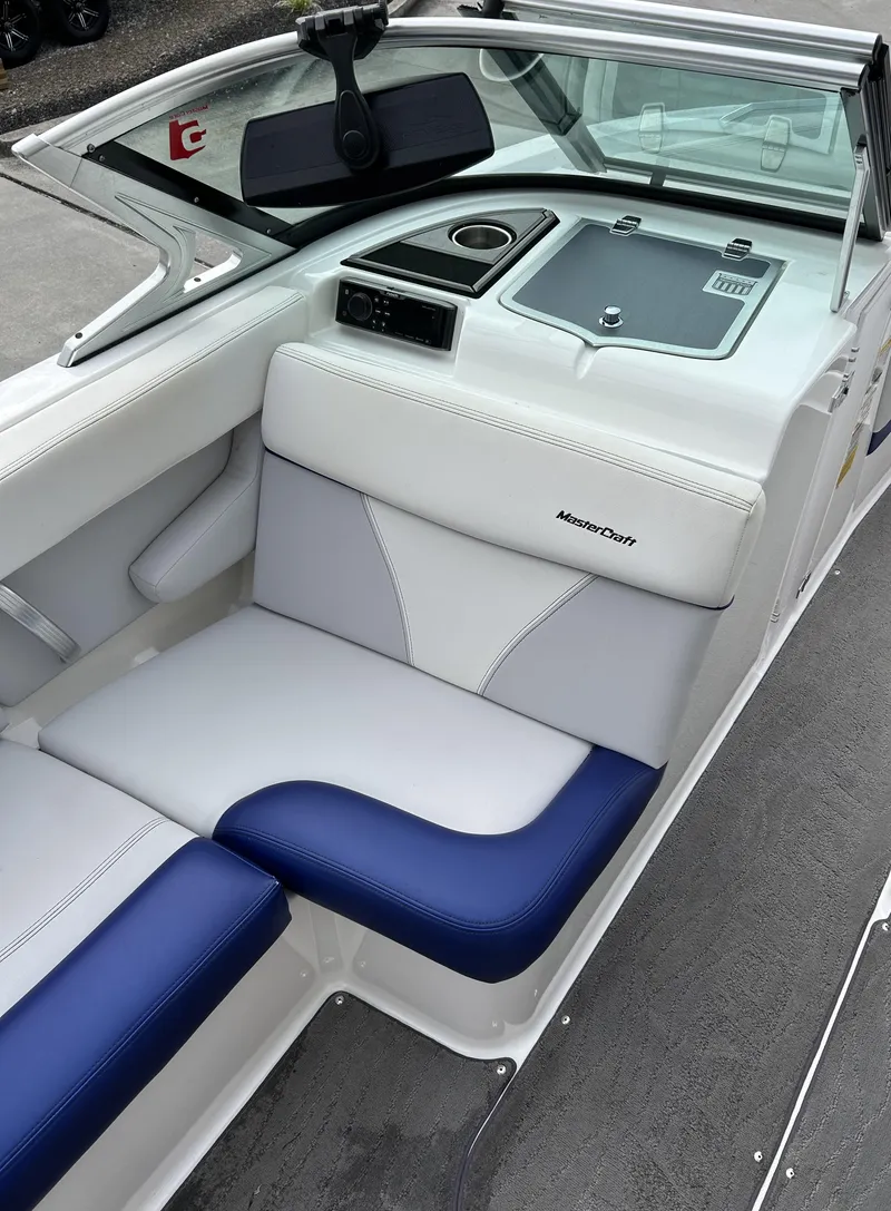 Slide: The Image of 2017 MasterCraft XT23 boat interior with white and blue seating, cup holder, and storage compartment. - 8