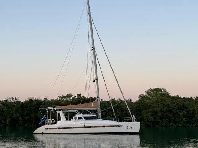 Slide: The Image of Voyage Yachts 500 catamaran, 2010 model, anchored near lush greenery at sunset. - 1