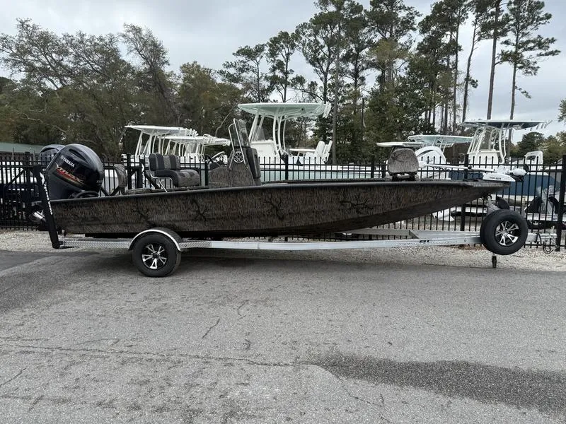 Slide: The Image of 2025 Xpress H22B Bay boat on trailer, parked outdoors near trees and other boats. - 1