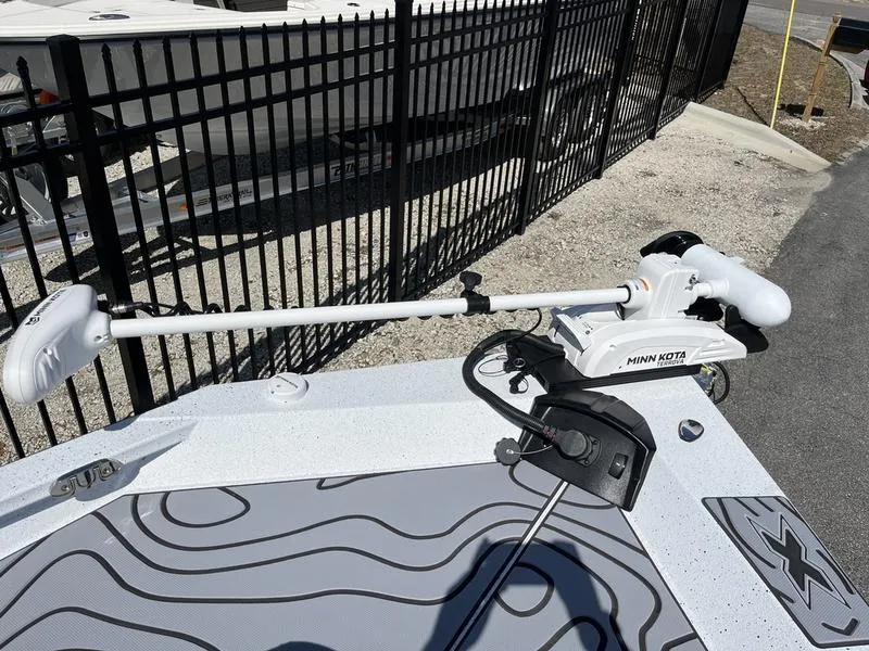 Slide: The Image of 2025 Xpress H22B boat with Minn Kota trolling motor, parked near a black fence. - 7