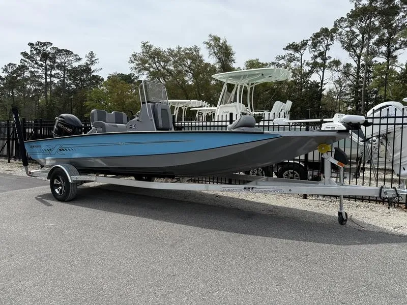 Slide: The Image of 2025 Xpress H20B boat on trailer, parked outdoors near a fence and trees. - 0