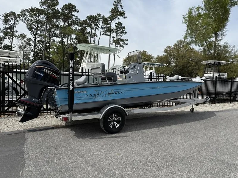Slide: The Image of 2025 Xpress H20B boat on trailer, blue hull, Yamaha outboard, parked near trees and fence. - 3