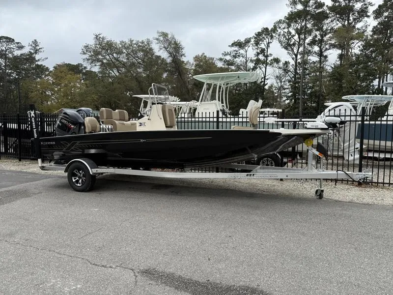 Slide: The Image of 2025 Xpress H20B boat on trailer, parked outdoors near other boats. - 0