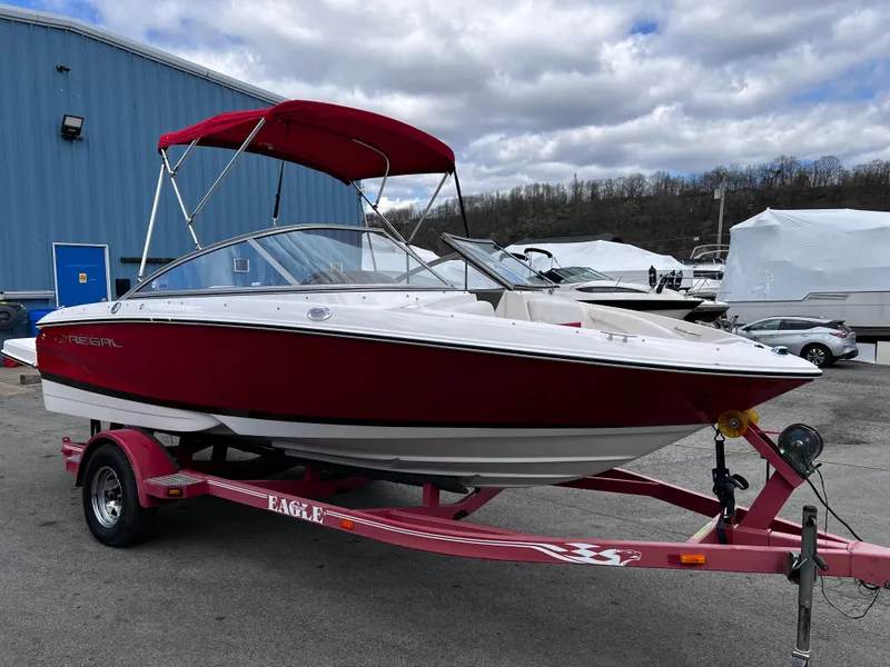 Slide: The Image of 2006 Regal 1900 Bowrider boat with red canopy on a trailer, parked outdoors. - 0