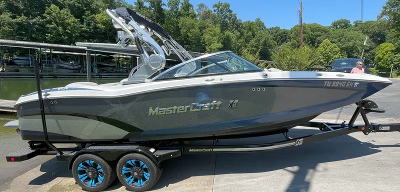 Slide: The Image of 2015 MasterCraft X23 boat on trailer, parked near a lake with lush greenery. - 4