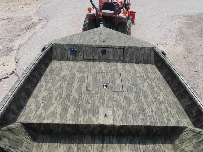 Slide: The Image of 2024 SeaArk Shadow 19v CC boat with camouflage design, viewed from above, near a tractor. - 9