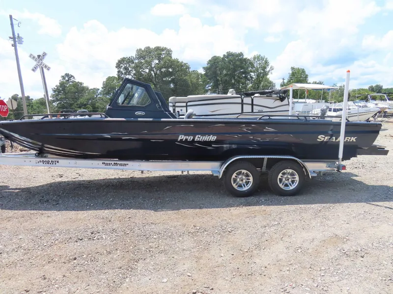 Slide: The Image of 2024 SeaArk Pro Guide 2672 boat on trailer, parked outdoors under a cloudy sky. - 17