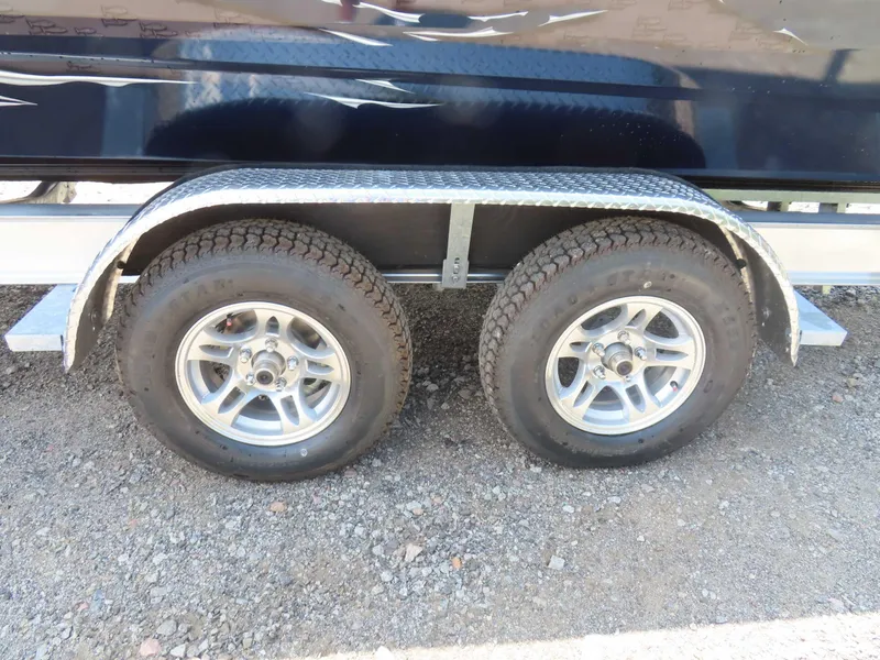 Slide: The Image of 2024 SeaArk Pro Guide 2672 trailer with dual wheels on gravel surface. - 18