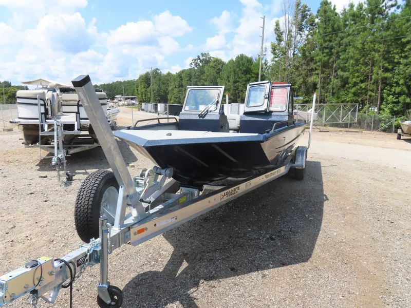 Slide: The Image of 2024 SeaArk Pro Guide 2672 boat on trailer, parked outdoors with trees in background. - 22