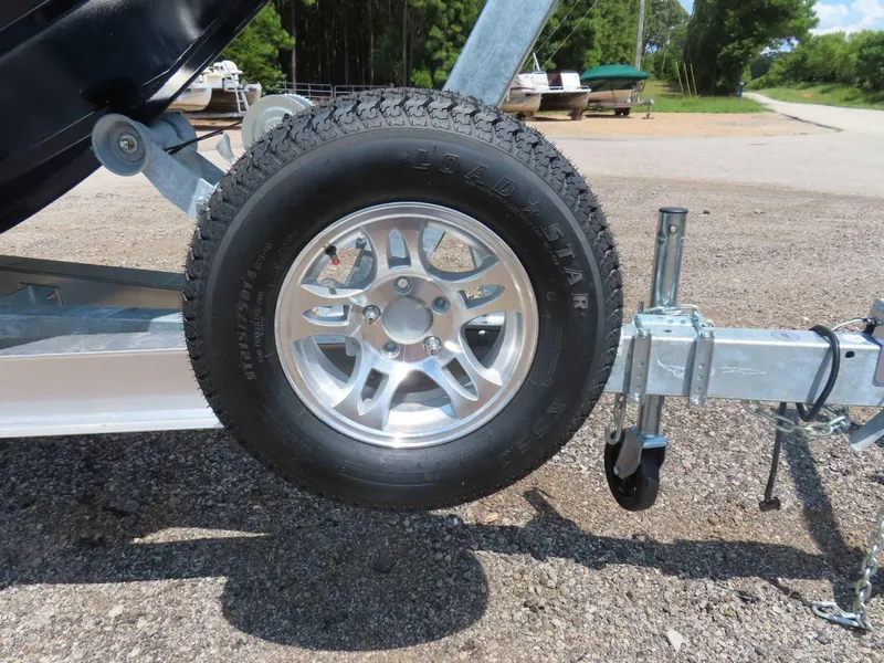 Slide: The Image of 2024 SeaArk Pro Guide 2672 trailer wheel on gravel, showcasing tire and rim details. - 23