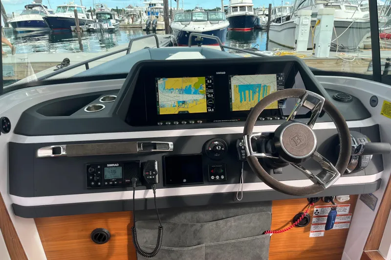 Slide: The Image of 2022 Axopar 28 Cabin Brabus Package dashboard with navigation screens, steering wheel, and marina view. - 19