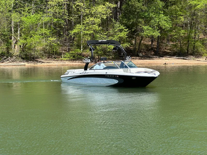 Slide: The Image of 2012 Centurion Enzo SV230 boat cruising on a serene lake with forested shoreline. - 2