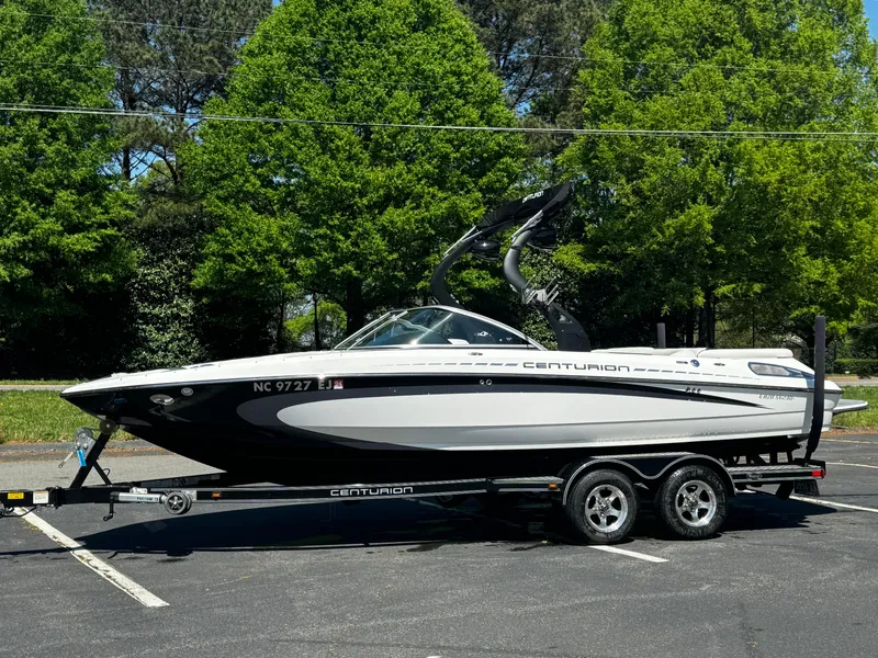 Slide: The Image of 2012 Centurion Enzo SV230 boat on trailer, parked in a lot with trees in the background. - 20