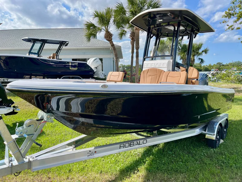 Slide: The Image of 2025 Robalo 226 Cayman boat on trailer, parked on grass with palm trees in background. - 4