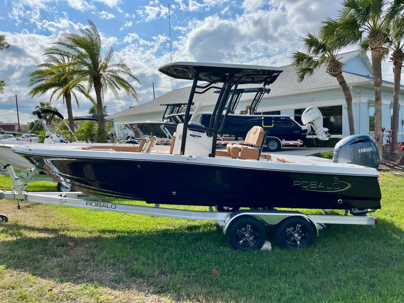 Slide: The Image of 2025 Robalo 226 Cayman boat on trailer, parked outdoors with palm trees and blue sky. - 5