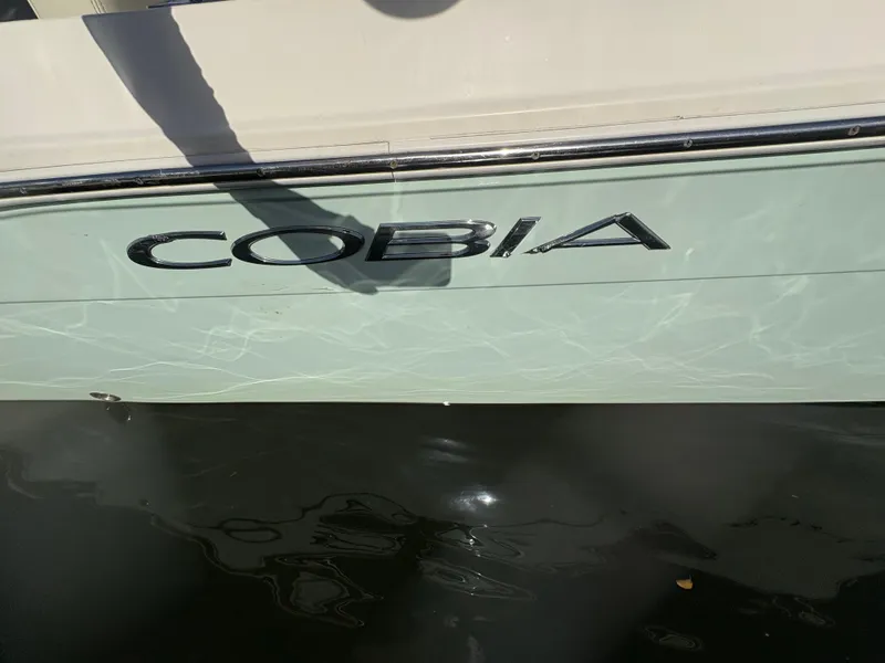 Slide: The Image of 2023 Cobia 237 CC boat side view with logo reflected on water. - 15