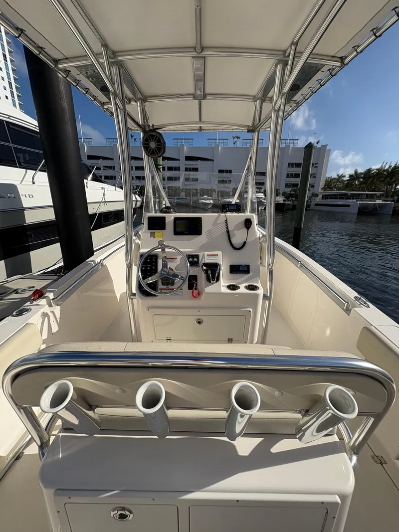 Slide: The Image of 2023 Cobia 237 CC boat interior with helm, rod holders, and marina backdrop. - 16