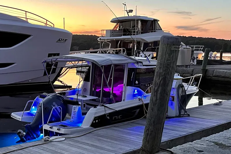 Slide: The Image of 2019 Jeanneau NC 795 boat docked at sunset with vibrant blue and purple lights. - 8