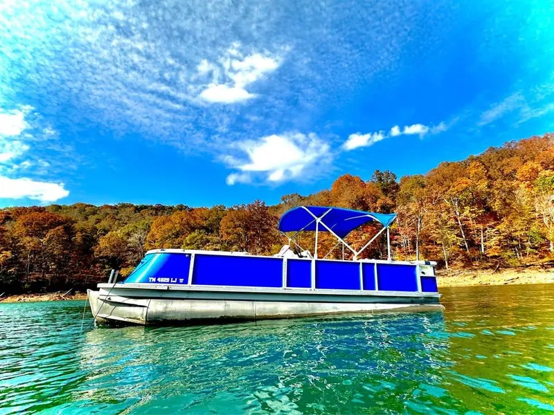 Slide: The Image of Pontoon boat on lake with blue canopy, surrounded by autumn trees under a clear sky. - 2