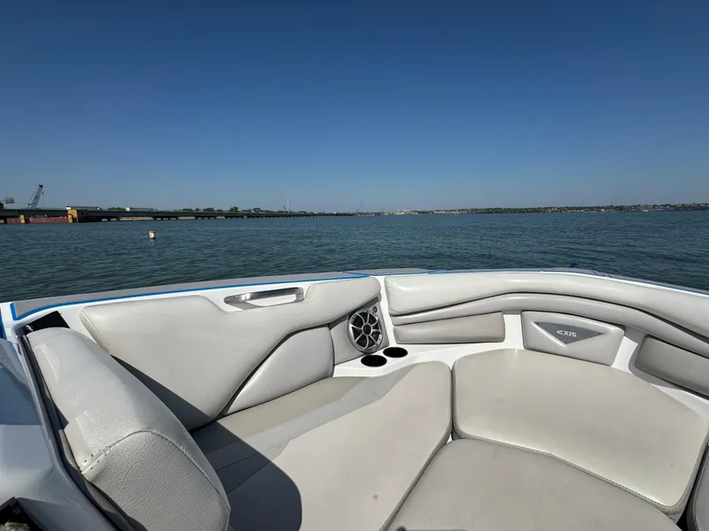 Slide: The Image of 2015 Axis A22 boat interior with gray seating, on a calm lake under clear blue sky. - 7