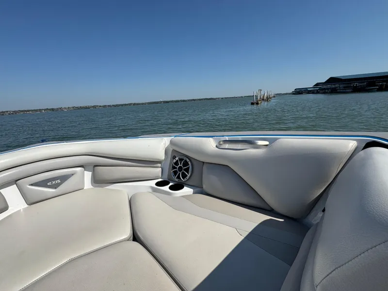 Slide: The Image of 2015 Axis A22 boat interior with gray seating, cup holders, and speaker, overlooking calm water. - 8