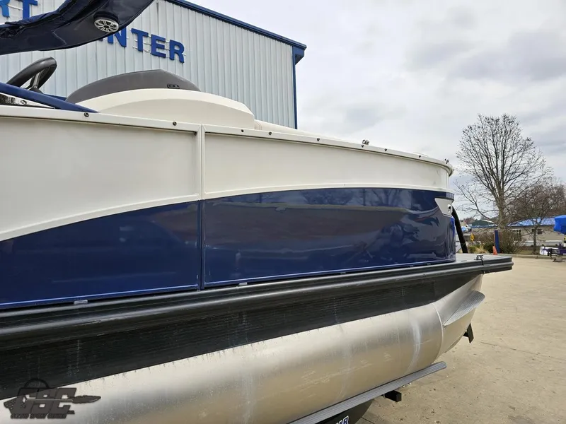 Slide: The Image of 2021 Bennington RX 25 Quad Bench pontoon boat, blue and white exterior, docked outdoors. - 10
