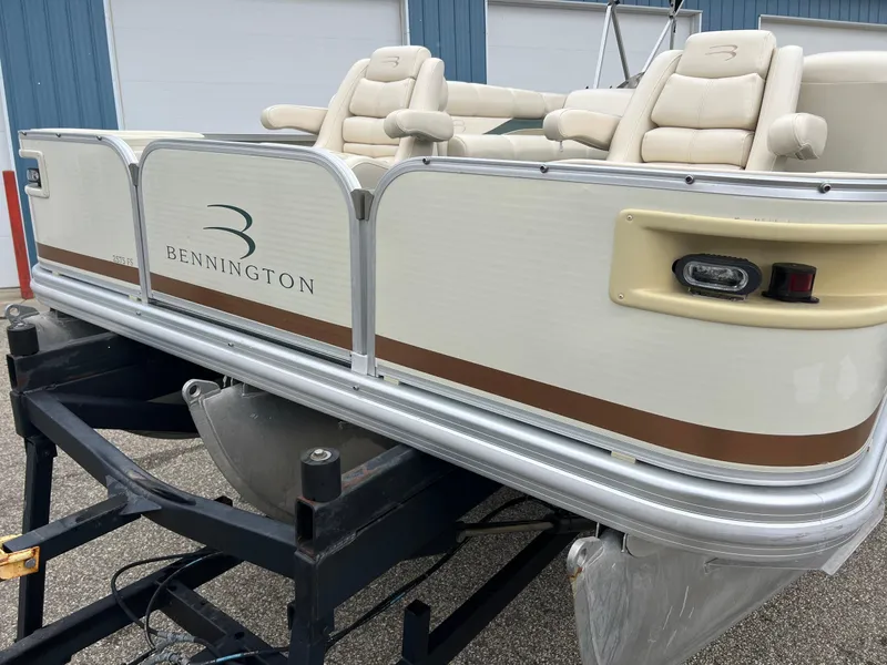 Slide: The Image of 2002 Bennington 2575 FS pontoon boat on trailer, beige seats, blue building background. - 46