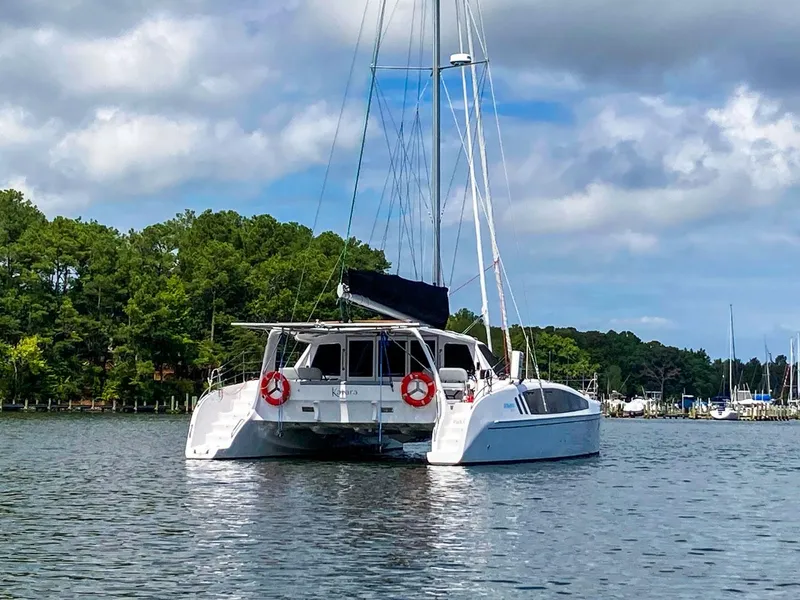 Slide: The Image of 2023 Seawind 1260 catamaran anchored on calm water with lush green trees in the background. - 2
