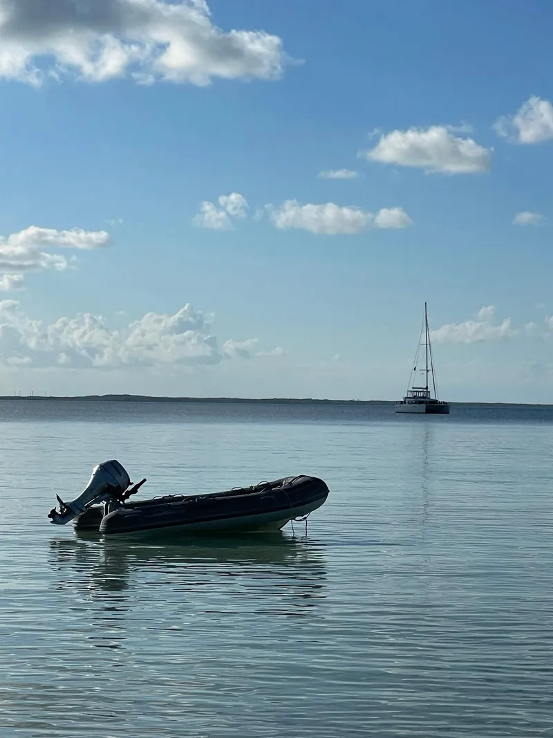 Slide: The Image of Inflatable boat on calm sea with Lagoon 450 F catamaran in the distance, under a blue sky. - 9