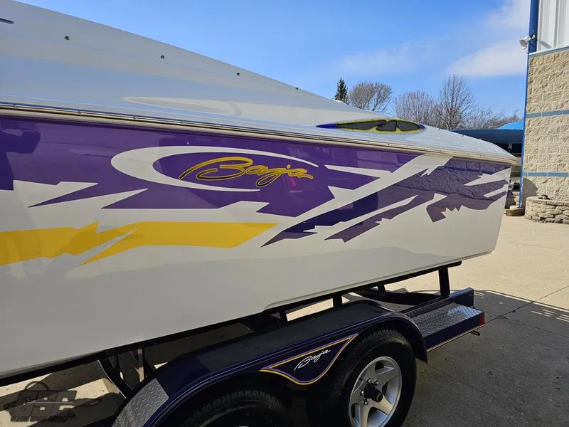Slide: The Image of 2004 Baja 25 Outlaw boat with vibrant purple and yellow graphics on a trailer. - 19